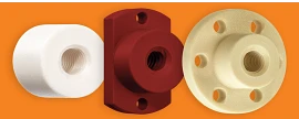 Three metric lead screw nuts lined up from left to right: the first is a white cylindrical nut with counterclockwise grooves spiraling inward. The second is a dark maroon cylindrical nut with a tall rectangular backing, featuring three holes—small holes at the top and bottom, and a larger hole with spiraling counterclockwise grooves. The third is a light tan cylindrical nut with a thinner backing, featuring six evenly spaced small holes and a large hole with counterclockwise grooves spiraling to the back.