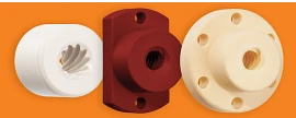 Three igus high helix lead screw nuts lined up from left to right: the first is a white cylindrical nut with counterclockwise grooves spiraling to the back and a hole at the center. The middle nut is dark maroon, with a tall rectangular backing featuring three holes—two small ones at the top and bottom, and a larger one with counterclockwise grooves. The third is light tan with a thinner cylindrical backing and six evenly spaced holes around its face, with grooves spiraling in the main cylinder.